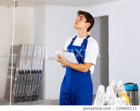 Focused contractor taking notes while planning renovation works in building 120660113