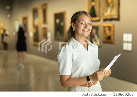 Woman with sheet piece of paper in hands view pictures and icons in museum hall Woman with sheet piece of paper in hands view pictures and icons in museum hall 120660202