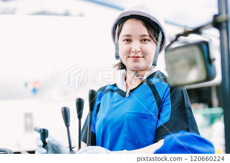 A woman in a helmet driving a forklift A woman in a helmet driving a forklift 120660224