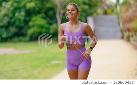 An Energetic Female Jogger Dressed in Purple Activewear Running on a Sunny Pathway 120660438