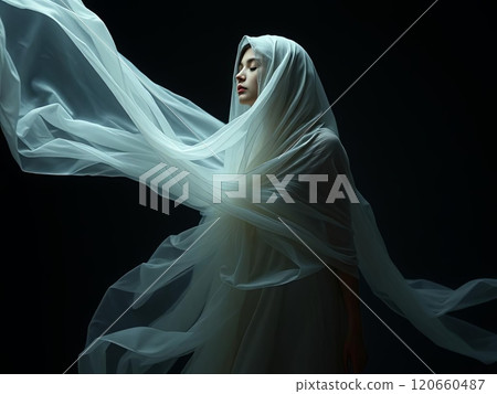 A woman dressed in a beautiful white gown is elegantly wrapped in a delicate white cloth, creating a striking visual appeal 120660487