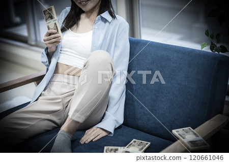 Laughing woman holding a stack of bills on the sofa 120661046