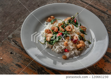 Rice topped with Stir fried thai basil with dwarf prawn served in white dish on wooden table, Thai Style food. Rice topped with Stir fried thai basil with dwarf prawn served in white dish on wooden table, Thai Style food. 120661230