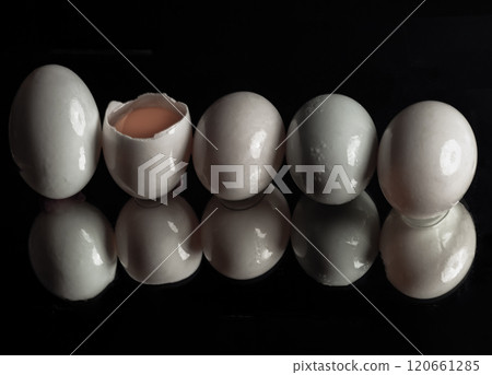 Five raw duck eggs are sitting in a row with an egg broken in half showing the yolk and white egg with reflection on dark background. 120661285