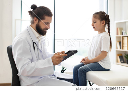 Doctor examines young girl and records medical data on tablet 120662517