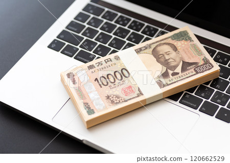 一疊新的 10,000 日元鈔票和一台放在黑色背景上的電腦 一疊新的 10,000 日元鈔票和一台放在黑色背景上的電腦 120662529