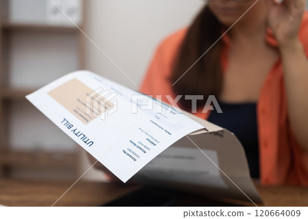woman studies utility statements earnestly, facing the daunting reality of increased expenses for electricity, water, and internet 120664009