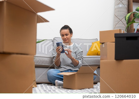 Celebrating Relocation: close up Young Woman Unpacks Boxes, Using Phone in Her Freshly Acquired Home 120664010