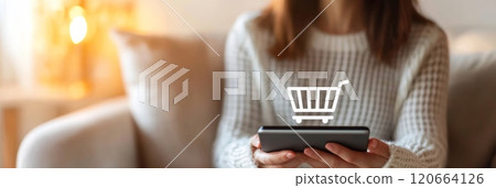 Woman is holding tablet and doing online shopping at home, with a shopping cart icon floating above the device, suggesting easy and convenient e commerce experience 120664126