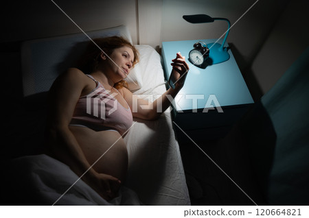 A pregnant woman lies in bed and uses a smartphone. Insomnia. 120664821