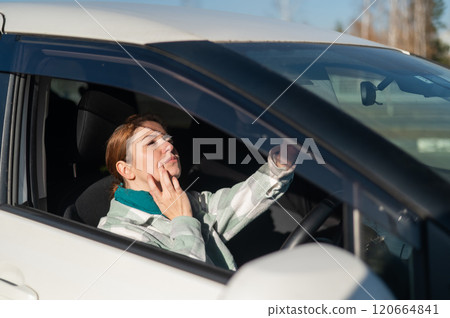 Caucasian woman sitting behind the wheel and looking in the mirror.  120664841