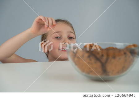 A little girl tries to steal cookies from the table. A little girl tries to steal cookies from the table. 120664945