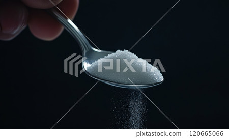 Hand holding a spoon pouring white refined sugar on dark background representing sugar addiction, unhealthy eating habits, diabetes, sugar reduction, and no added sugar lifestyle 120665066