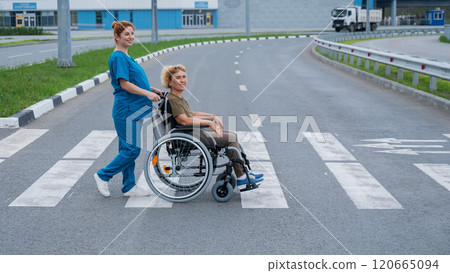 Red-haired nurse pushing an elderly woman in a wheelchair across the road.  120665094
