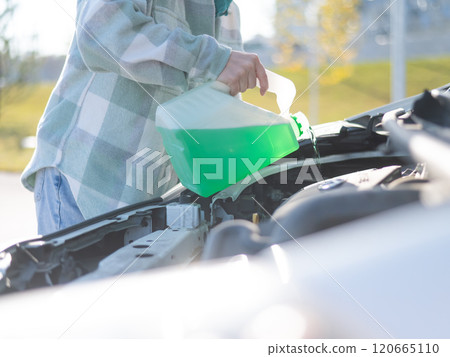 Close up of female hands filling car reservoir with windshield washer fluid from bottle.  120665110