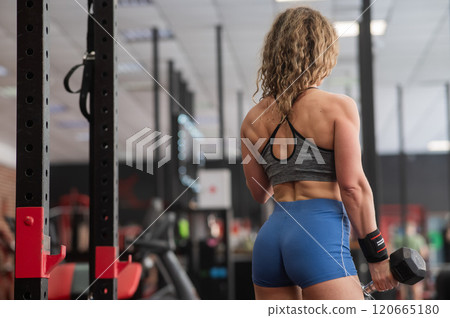 Muscular Caucasian forty year old woman doing exercises with dumbbells in the gym.  120665180
