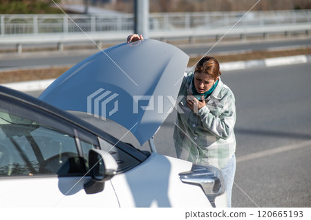 Caucasian woman looks puzzled under the hood of a car.  120665193