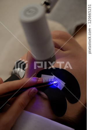 A woman undergoing eyelash extension procedure using an ultraviolet lamp. A woman undergoing eyelash extension procedure using an ultraviolet lamp. 120665231