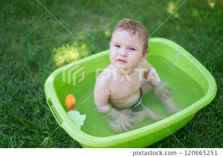 Cute baby boy bathes in a basin outdoors in summer. 120665251