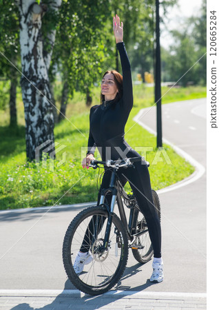 Caucasian woman riding a bike in a park. Vertical photo.  120665284