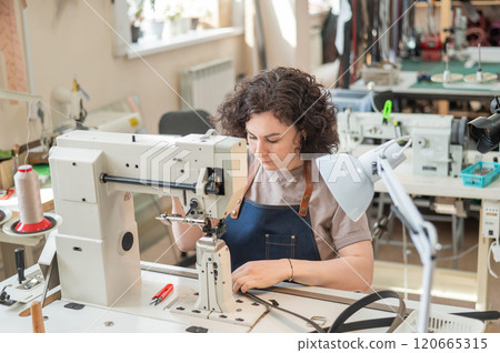 A woman tanner sews a leather belt on a sewing machine. A woman tanner sews a leather belt on a sewing machine. 120665315