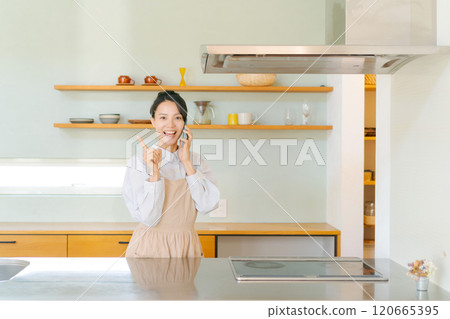 Woman talking on smartphone in kitchen Woman talking on smartphone in kitchen 120665395