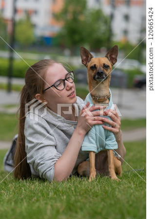 Young Caucasian woman lying on the lawn while walking with a small dog.  Young Caucasian woman lying on the lawn while walking with a small dog.  120665424