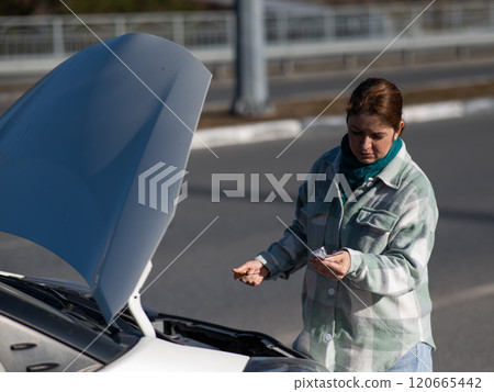 Caucasian female driver checking oil level in car engine.  120665442