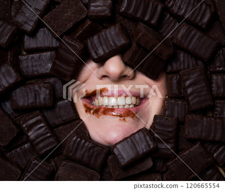 The face of a caucasian woman surrounded by sweets. The girl is smeared in chocolate.  120665554