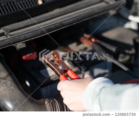 Woman holding clamps for charging a car battery. Woman holding clamps for charging a car battery. 120665730