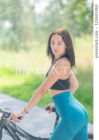 Caucasian woman riding a bike in a park. Vertical photo.  120665868