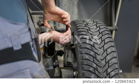 Mechanic removes wheel balance weight from car wheel. Mechanic removes wheel balance weight from car wheel. 120665925