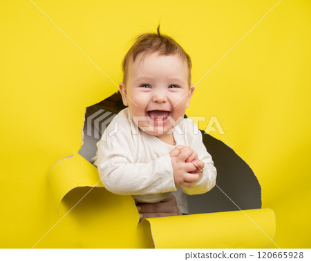 Cheerful baby rips and sticks out through yellow cardboard background.  120665928