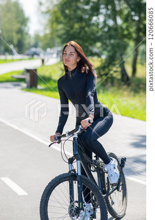 Caucasian woman riding a bike in a park. Vertical photo.  120666085