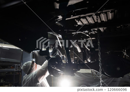 An auto mechanic applies anti-corrosion mastic to the underbody of a car. An auto mechanic applies anti-corrosion mastic to the underbody of a car. 120666096