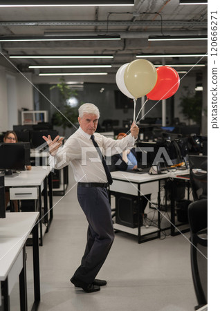 Portrait of a cheerful mature business man holding balloons in the office. Vertical photo.  120666271