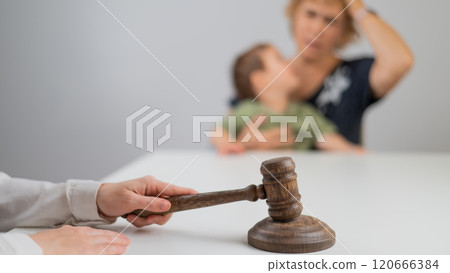 A judge hits a gavel against the backdrop of an elderly woman holding a child.  120666384
