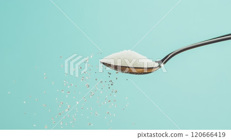 Falling sugar from spoon on turquoise background, symbolizing sugar reduction and health risks 120666419