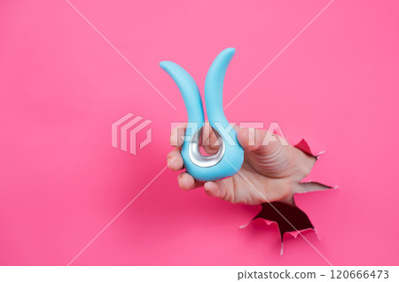 Female hand sticking out of pink paper background with blue curved vibrator sex toy.  120666473