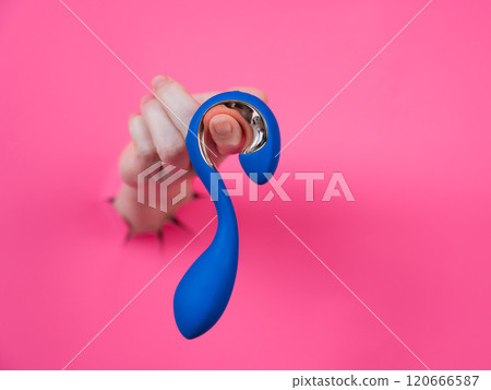 Hand with blue vibrator sticking out through pink paper background. Hand with blue vibrator sticking out through pink paper background. 120666587
