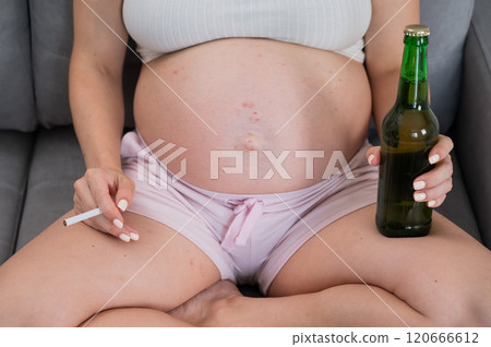 Faceless pregnant woman drinks beer while sitting on the sofa. Faceless pregnant woman drinks beer while sitting on the sofa. 120666612