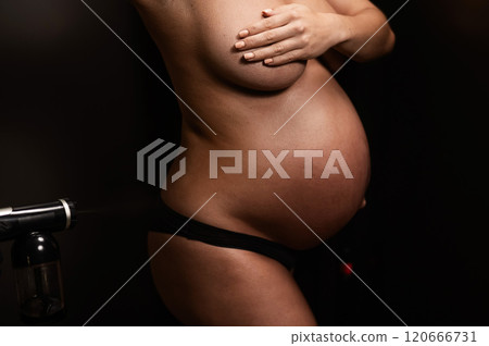 Faceless pregnant woman getting an instant tan. The master applies bronzer with a spray. Faceless pregnant woman getting an instant tan. The master applies bronzer with a spray. 120666731