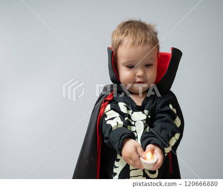 Little Caucasian boy in Dracula costume holding candle on white background.  120666880
