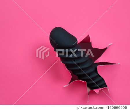 Black ribbed dildo sticking out of hole on pink background.  120666906