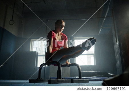 Athletic young woman perfectly performing L sit on planche bars while working out in gym with gymnastics equipment, copy space 120667191