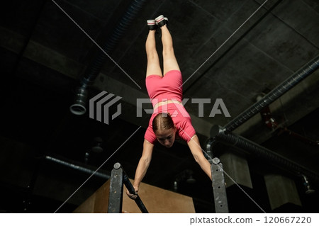 Low angle shot of professional female athlete in handstand on parallel bars balancing with body straight while mastering gymnastic technique against high gym ceiling, copy space Low angle shot of professional female athlete in handstand on parallel bars balancing with body straight while mastering gymnastic technique against high gym ceiling, copy space 120667220