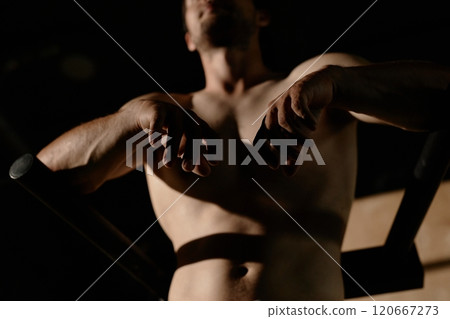 Close up on hands of fit shirtless man with arms resting on parallel bars captured during workout in gym with low key lightning, copy space 120667273