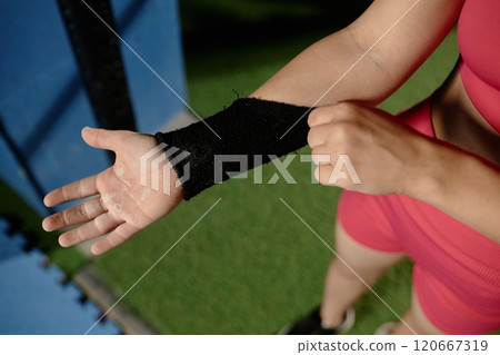 Close up on hands in magnesia powder of unrecognizable female gymnast putting on sweatband to protect wrist while preparing to practice bar routines in gym, copy space 120667319