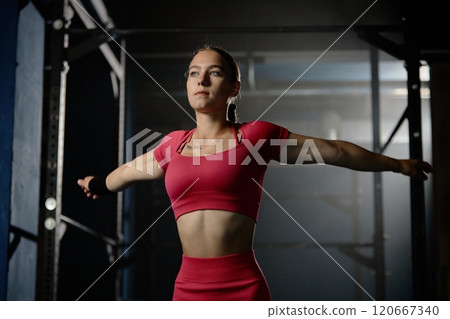 Medium shot of young fit woman wearing pink workout set of matching crop top and shorts stretching arm muscles while warming up before training on high bar in gym, copy space Medium shot of young fit woman wearing pink workout set of matching crop top and shorts stretching arm muscles while warming up before training on high bar in gym, copy space 120667340