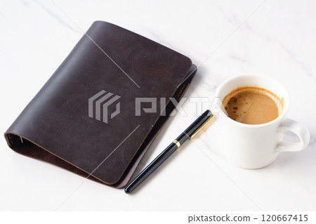 Image of a man working at his desk with a brown leather organizer while drinking a cafe latte, a coffee with milk 120667415